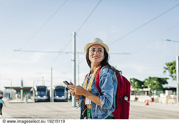 Happy young woman with mobile phone standing on sunny day