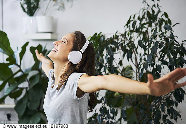 Happy young woman with oustretched arms listening to music at indoor plant