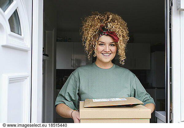 Happy young woman with packages standing at doorway