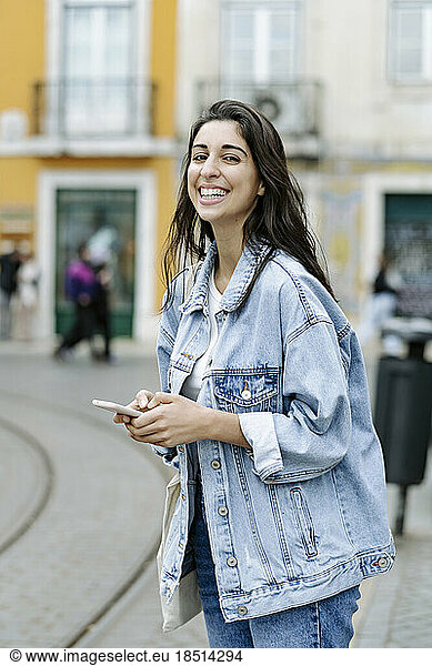 Happy young woman with smart phone standing in city