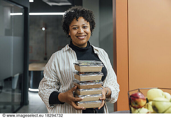 Happy young woman with take away food boxes standing in office