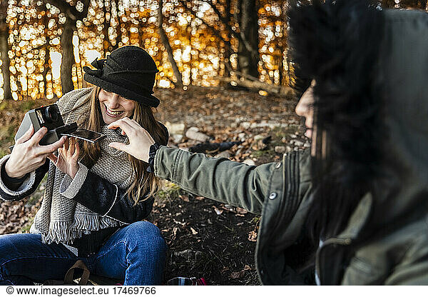 Happy young women taking photographs in autumn forest