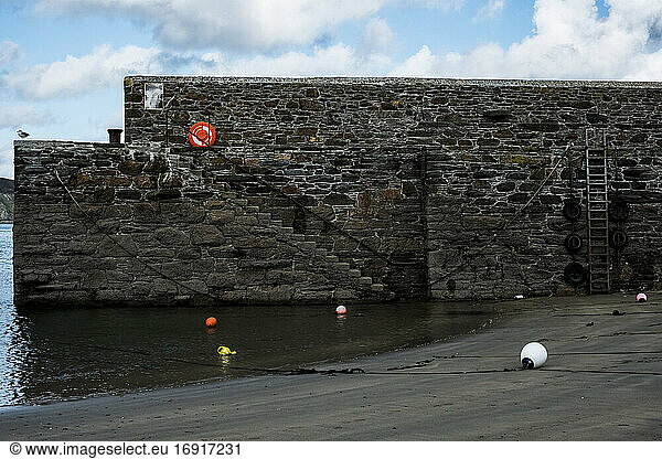 Harbour wall with stairs and buoys on sand at low tide.