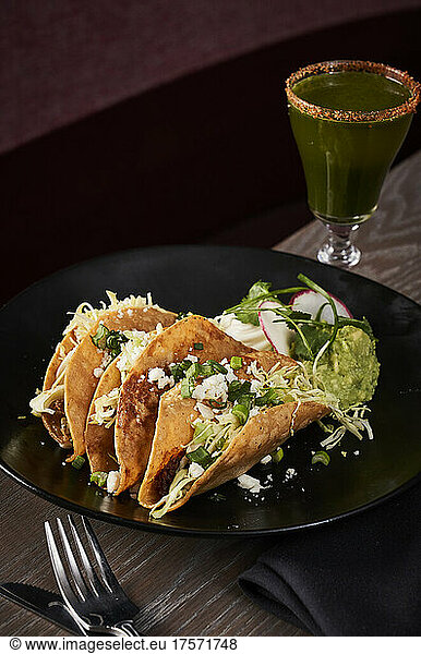 Hard shelled tacos with guacamole and a craft cocktail .