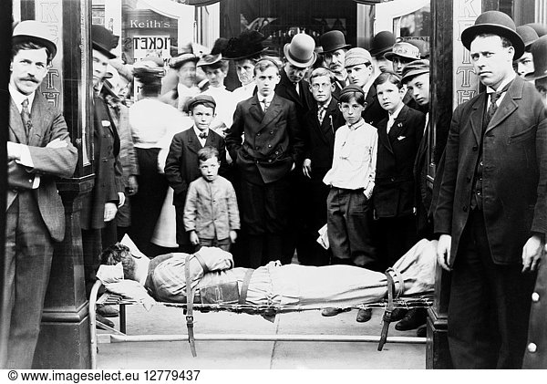 HARRY HOUDINI (1874-1926). American magician. Houdini strapped to a cot  with an audience surrounding him. Photograph  c1915.