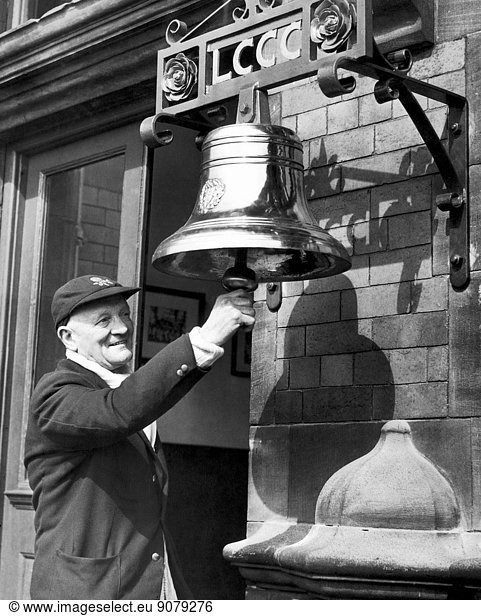 Harry Makepeace rings the bell to beging the new season. The old bell has been cleaned and hung on a new frame outtside the entrance to the pavillion at Lancashire County Cricket Club. 18th April 1951.