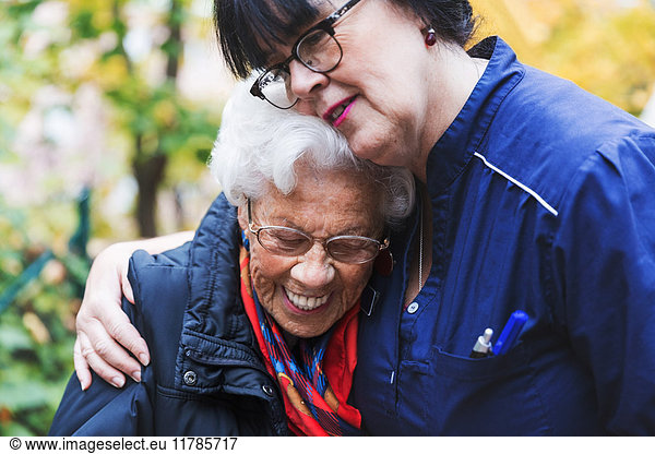 Hausmeisterin umarmt Seniorin im Park