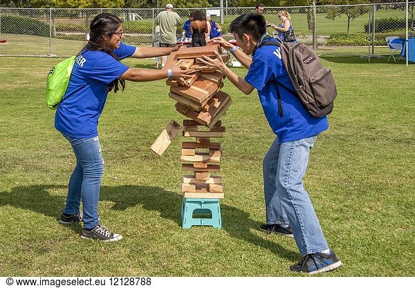 Having piled their Giant Jenga stack a little too high  two Asian American teens try to catch the falling wood blocks at an outdoor festival in Fountain Valley  CA.