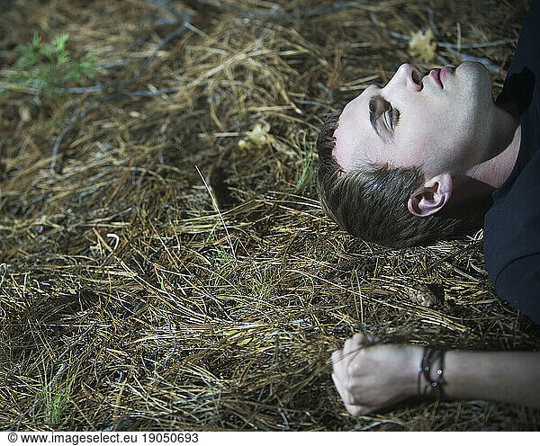 Head and arm of a young man lying on the ground outside.