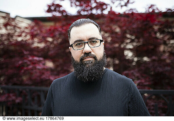 Headshot of a bearded man with glasses in front of a red maple tree