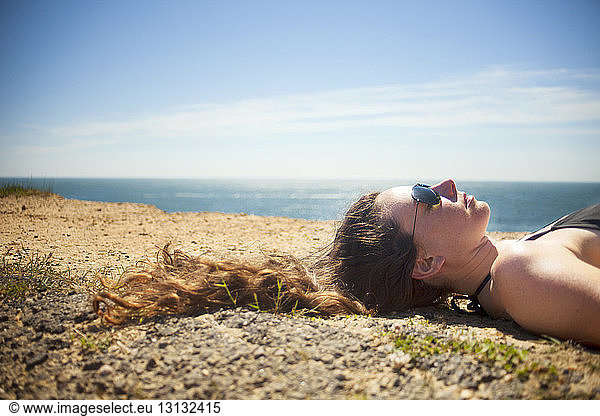 Headshot of woman lying on sand against sky