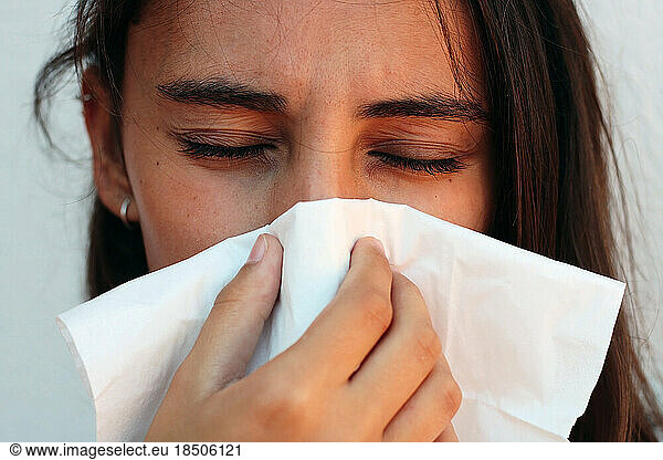 Health and medicine concept - Young woman blowing nose into tissue.