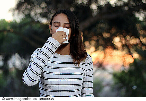 Health and medicine concept - Young woman blowing nose into tissue.