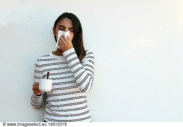 Health and medicine concept - Young woman blowing nose into tissue.