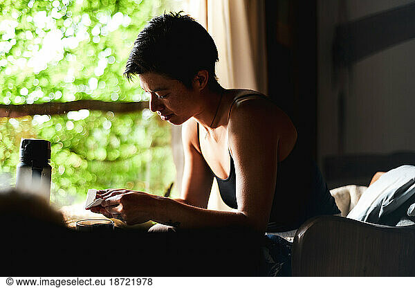 healthy asian woman sits inside her wooden home by window light green