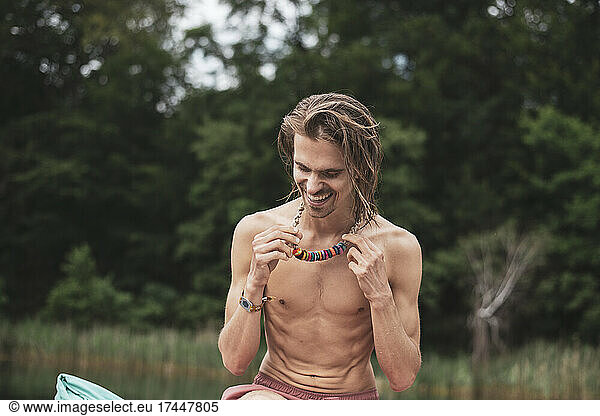 Healthy bohemian man laughs with colourful necklace by natural lake