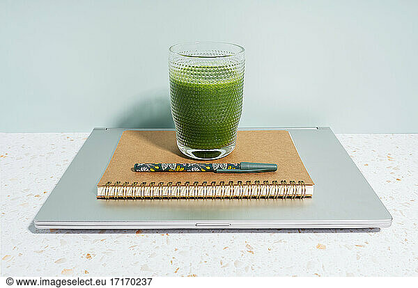 Healthy green juice  book  pen and laptop over desk against wall