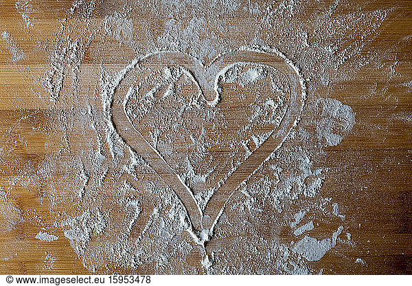 Heart shape made with flour on wooden board