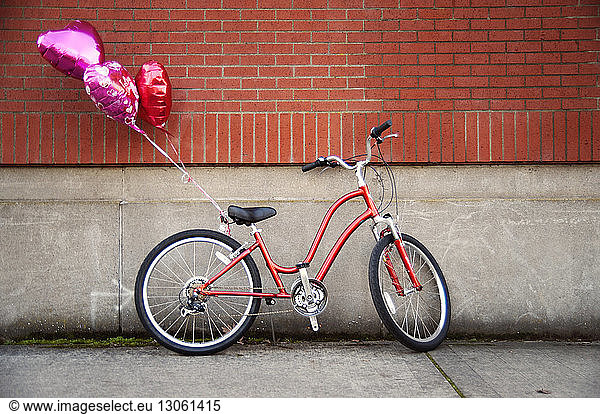 Heart shaped balloons tied to bicycle parked against wall