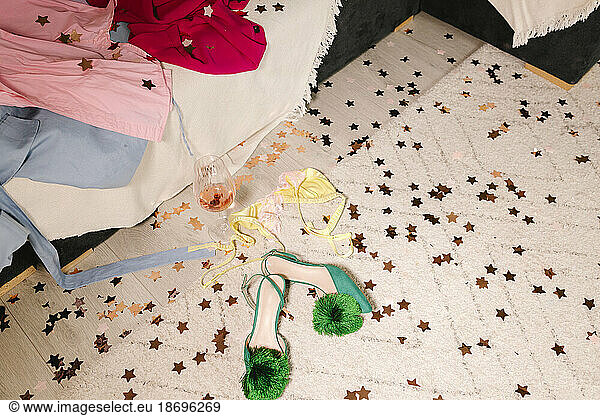 Heels by wineglass and dress on carpet with confetti at home