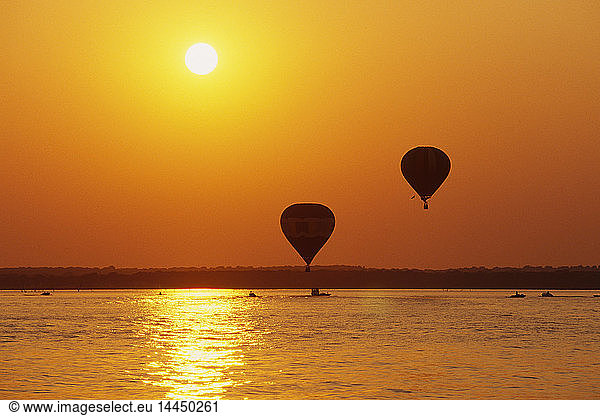 Heißluftballons über Wasser bei Sonnenuntergang