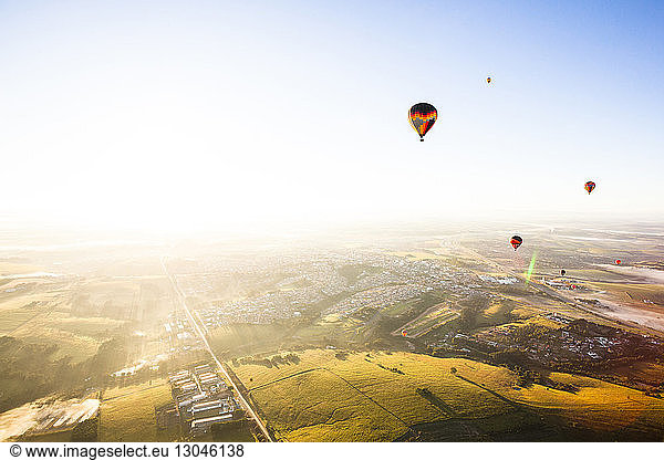 Heissluftballons fliegen bei Sonnenschein über die Landschaft gegen den klaren Himmel