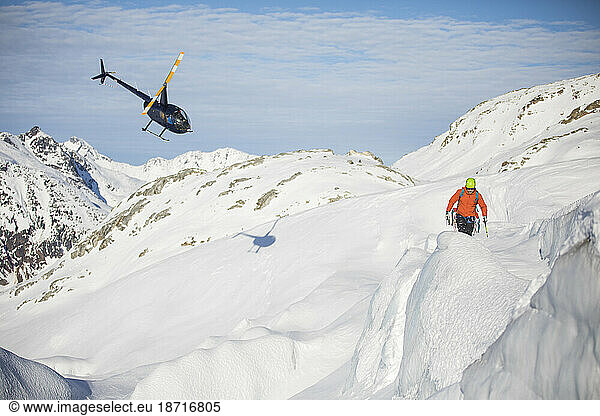 Helicopter approaches mountaineer in a mountain landscape.