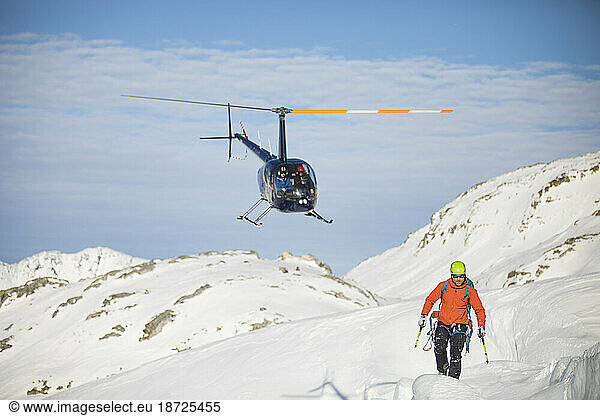Helicopter approaches mountaineer in a snowy landscape.