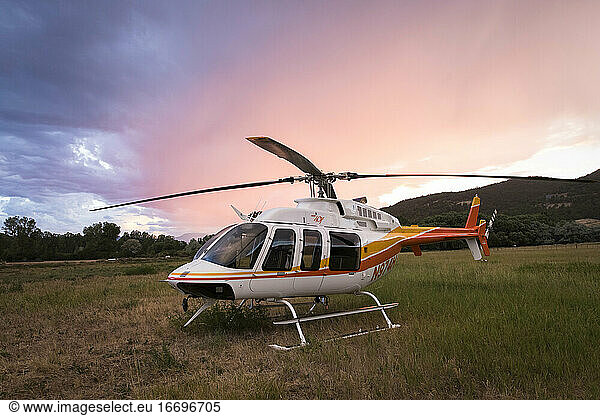 Helicopter on field against cloudy sky during sunset