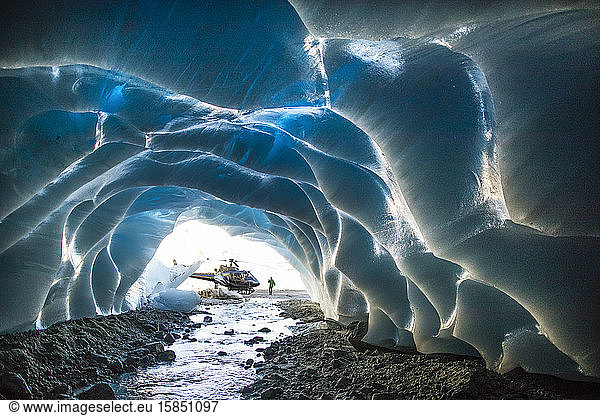 Helicopter parked next to entrance of ice cave during luxury tour.