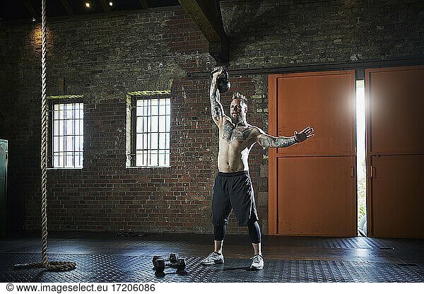 Hemdloser männlicher Athlet  der eine Kettlebell hebt  während er im Fitnessstudio trainiert