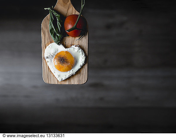 Herzförmiges Sonnenseite-oben-Ei und Tomate auf Schneidebrett