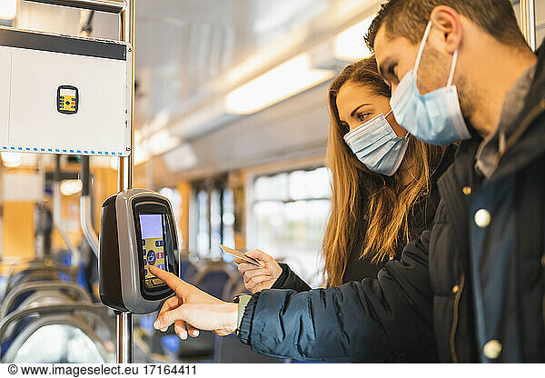 Heterosexual couple doing contactless payment while commuting through tram during pandemic