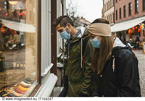 Heterosexual couple doing window shopping while standing outside store during pandemic