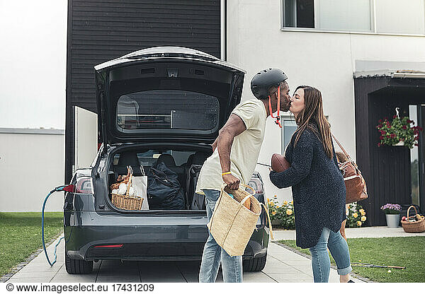 Heterosexual couple kissing while standing by electric car