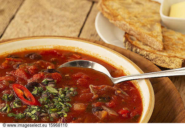 High angle close up bowl of tomato and vegetable soup with side order of bread in a cafe.