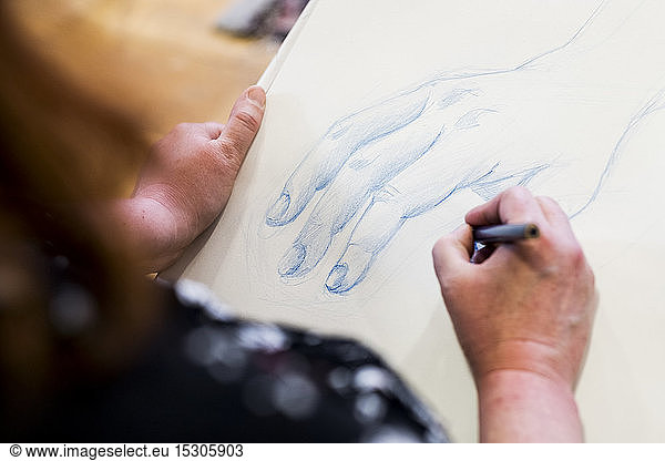 High angle close up of artist drawing human hand.