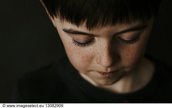 High angle close-up of boy with freckles over black background