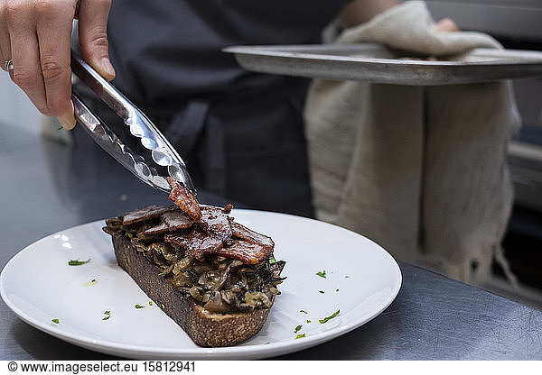 High angle close up of chef preparing toasted bread with bacon and mushrooms in an artisan bakery.
