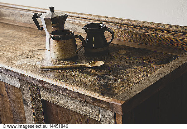 High angle close up of Espresso maker  earthenware mug and jug and wooden spoon on vintage wooden kitchen cupboard.