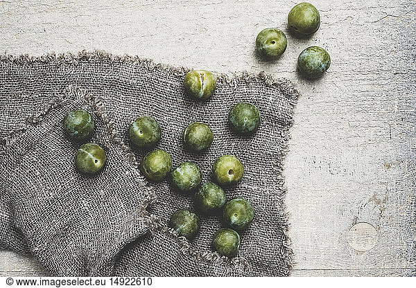 High angle close up of fresh greengages on grey cloth.