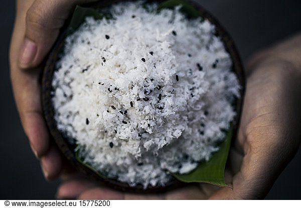 High angle close up of hand holding coconut flesh and black sesame seeds used as a body scrub.