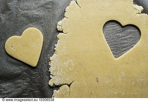 High angle close up of heart-shaped cookies cut out of cookie dough on a grey background.