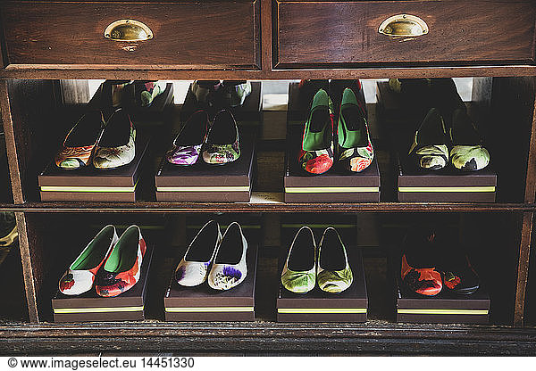 High angle close up of heeled shoes with colourful floral patterns on brown boxes lined up on wooden shelves.