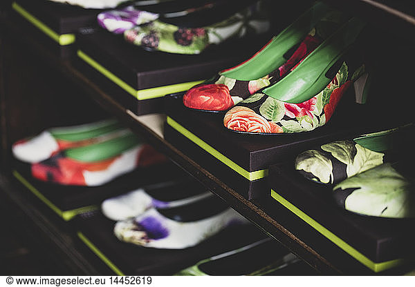 High angle close up of heeled shoes with colourful floral patterns on brown boxes lined up on wooden shelves.