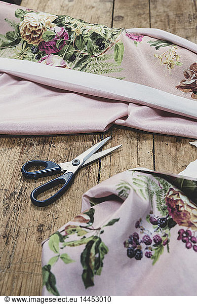 High angle close up of pair of scissors and pink fabric with floral pattern on wooden table.