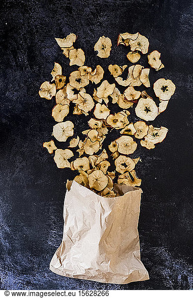 High angle close up of paper bag and dried slices of apple on dark background.