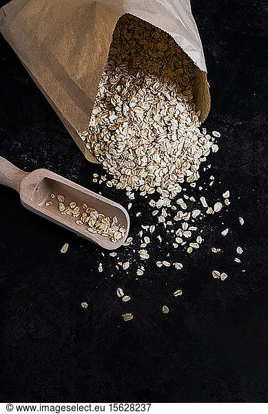 High angle close up of paper bag with oats and wooden spoon on dark background.