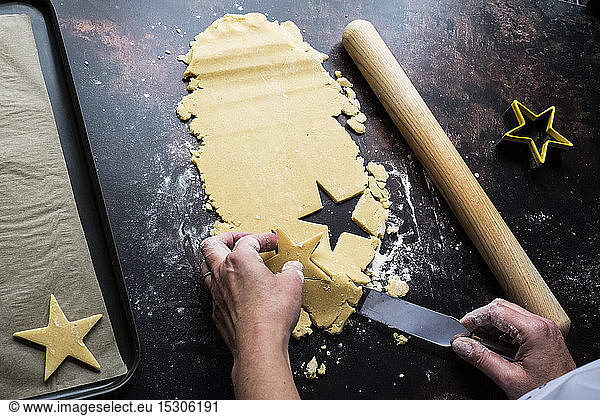 High angle close up of person lifting cut out star-shaped cookies onto a baking tray with a palette knife.