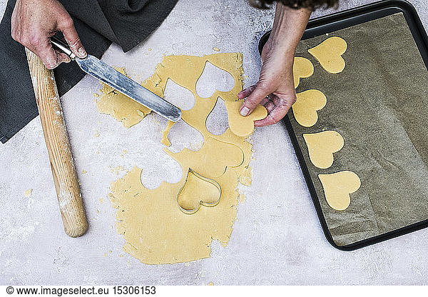 High angle close up of person using palette knife to move heart-shaped cookies onto a baking tray.